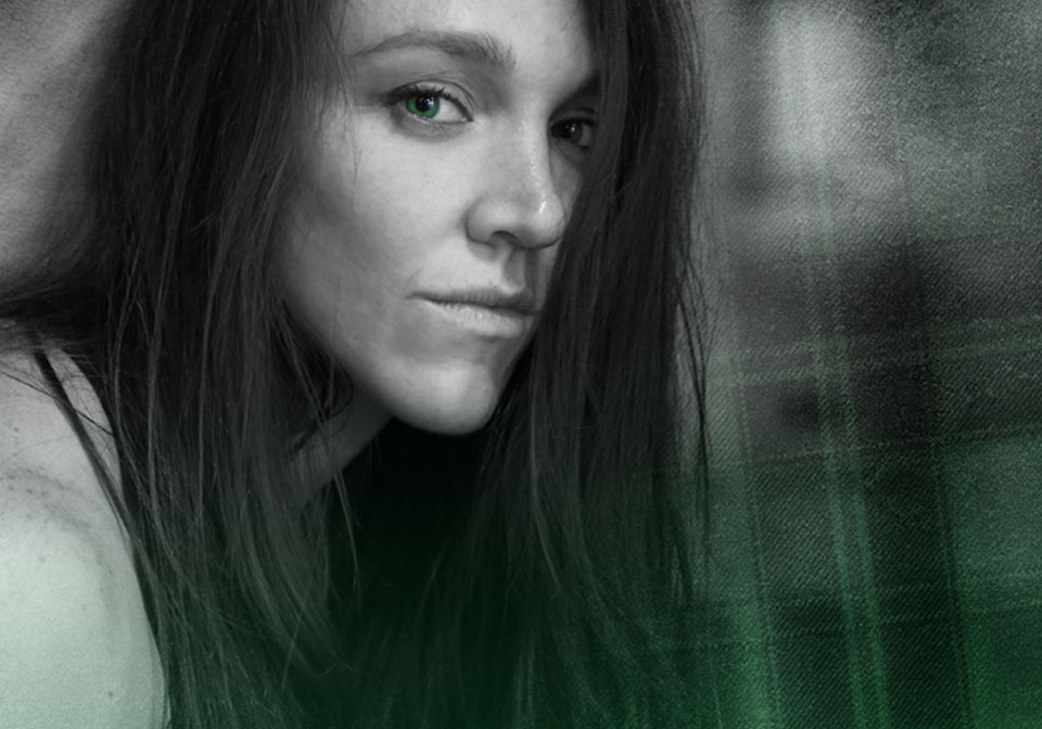 Black and white photo of a woman with a green eye looking outward and a tartan background.